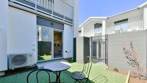 Ein Wohngebäude mit Balkon, einer kleinen Terrasse mit Tisch und Stühlen sowie einem umzäunten Garten.