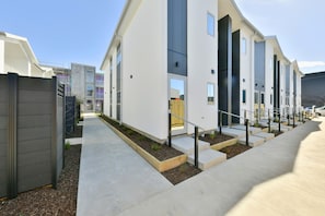 Un moderno edificio residencial con techo plano, amplias ventanas y entrada protegida por una reja.