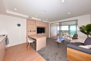 A modern apartment with a kitchenette, a dining area, a living room with a sofa, and a balcony with a view.