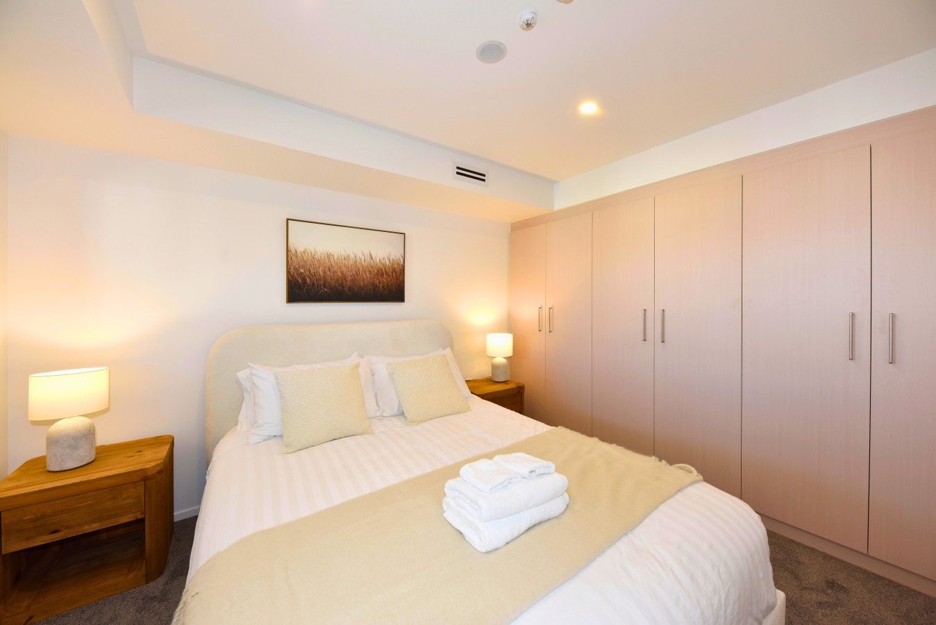 A bedroom with a bed, bedside lamps, a wall-mounted picture, and a wardrobe.
