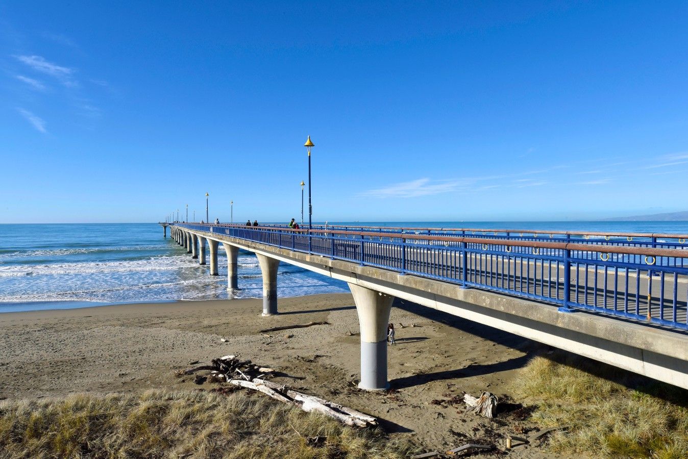 A coastal pier with a blue railing, concrete supports, and a clear sky.