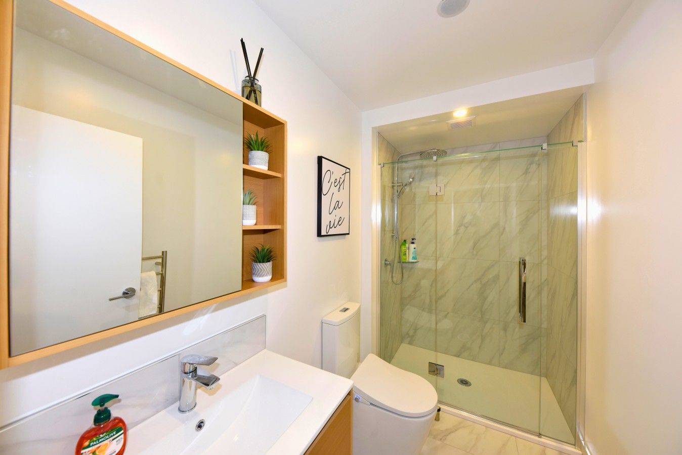 A modern bathroom with a large mirror, a sink, a toilet, and a glass-enclosed shower.
