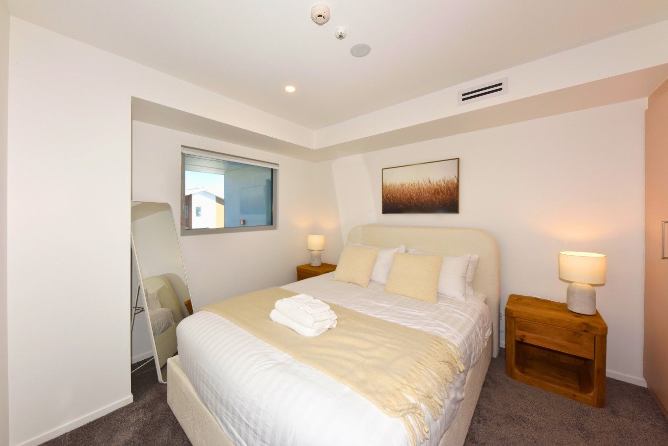A hotel room with a bed, bedside lamps, a window, and a painting on the wall.