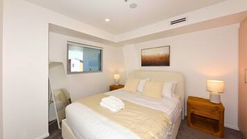 A hotel room with a bed, bedside lamps, a window, and a painting on the wall.