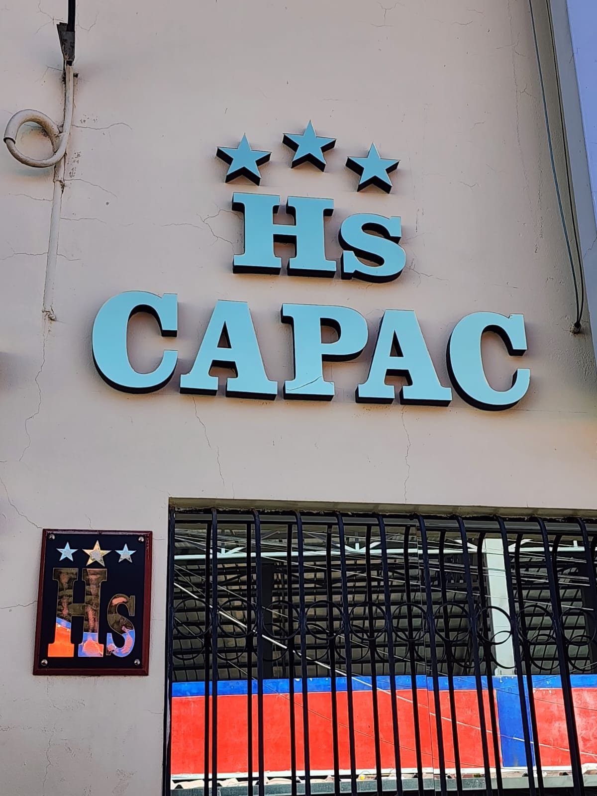 A building with a sign that reads 'Hs CAPAC' and a window with a metal grill.