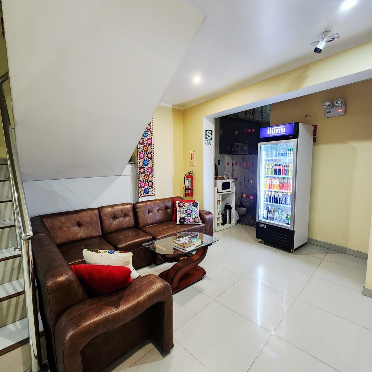 A living room with a brown leather sofa, a glass coffee table, and a refrigerator stocked with beverages.
