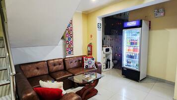 Sala de estar com sofá de couro marrom, mesa de centro de vidro e uma geladeira abastecida com bebidas.