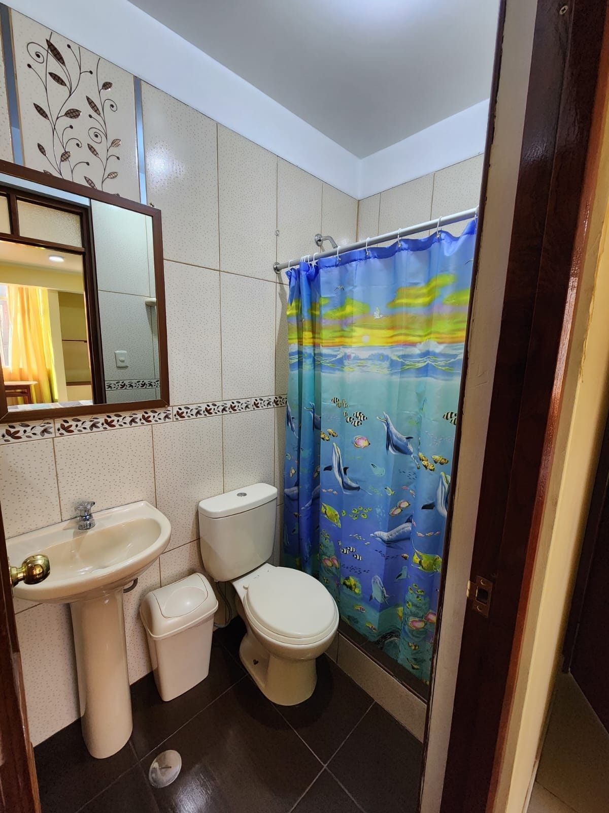 Un baño con lavamanos, dos inodoros, un espejo y una cortina de ducha con motivos marinos.