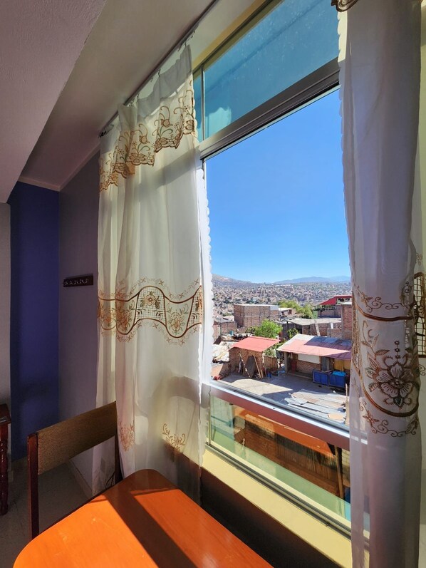 A room with a view of a cityscape through a window with decorative curtains.