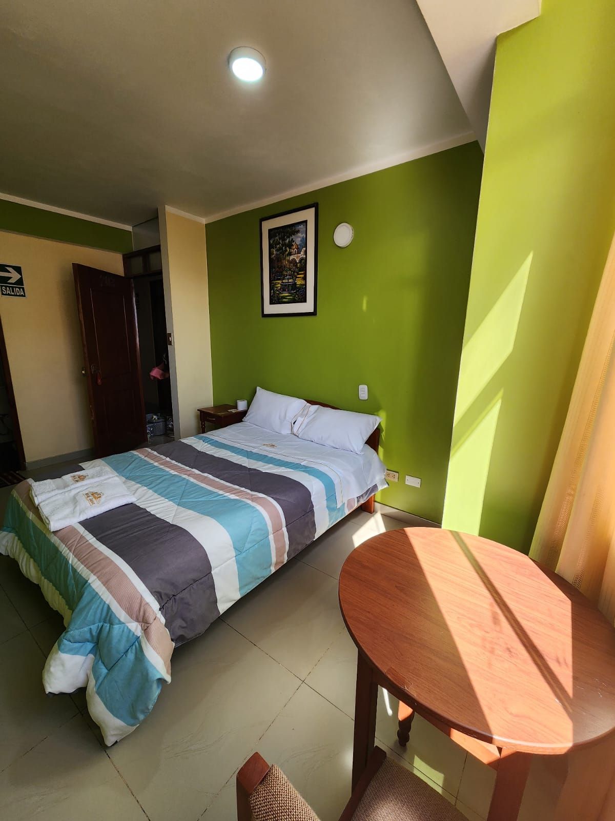 Un dormitorio con cama, mesita de noche, una mesa de madera y pared verde.