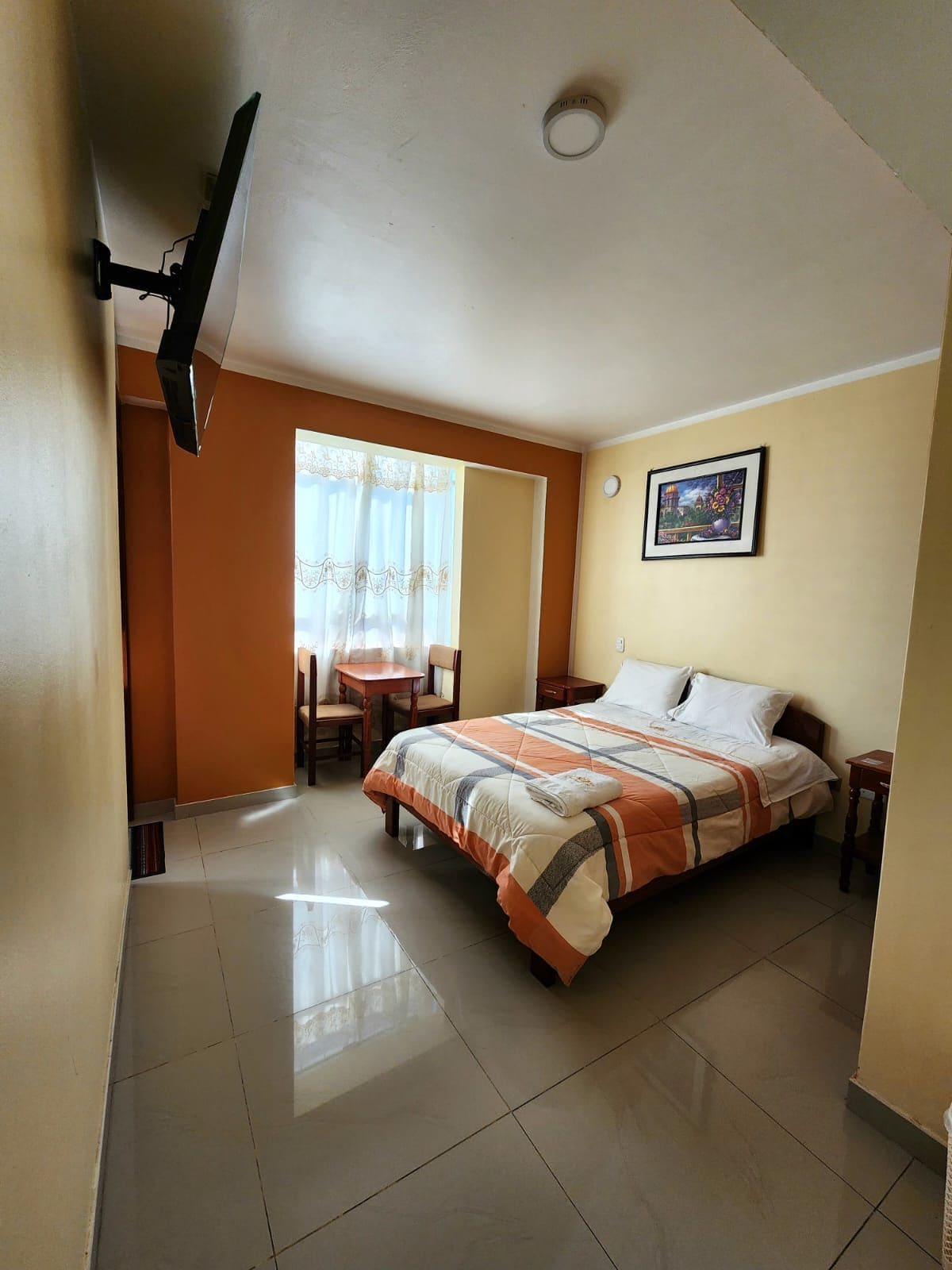 Een hotelkamer met een bed, een bureau, een stoel, een raam met gordijnen en een schilderij aan de muur.