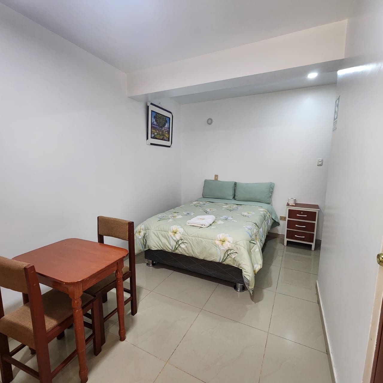 A small, clean room with a bed, a wooden table, and a chair.