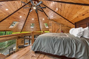 A bedroom with a sloped ceiling, a bed with pillows, a skylight, and a view of greenery outside.