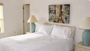 Een slaapkamer met een bed, twee nachtkastjes, een nachtkastje, een deur en een schilderij van de Eiffeltoren.