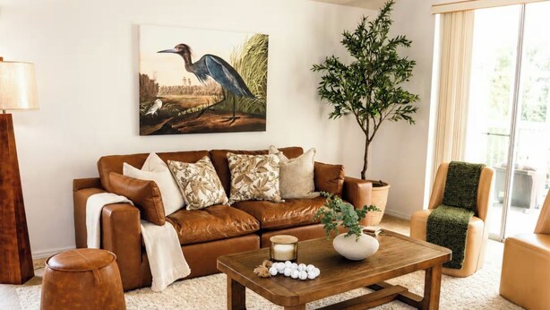 Een woonkamer met een bruine leren bank, een houten salontafel en een groot schilderij van een vogel.