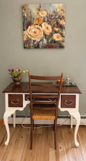 A wooden desk with drawers, a chair, and a painting on the wall.