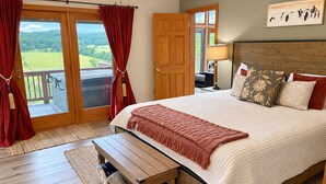 Un dormitorio con una cama grande, cabecera de madera, un banco y vista al exterior a través de una puerta corredera, además de un cuadro en la pared.