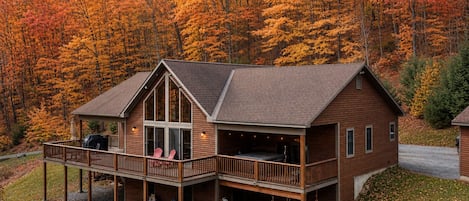 A two-story wooden cabin with a balcony, surrounded by autumn foliage.