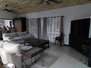 A living room with a sofa, a coffee table, a television, and a ceiling fan. - The Garden Inn (Sinton)