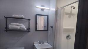 Et badeværelse med toilet, vask, brusebad, håndklædestige og et spejl.