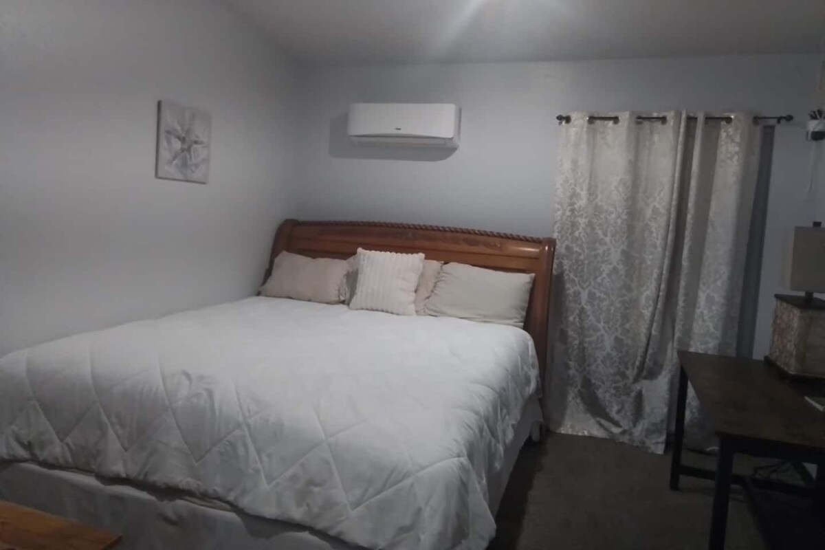A bedroom with a bed, a bedside table, a lamp, and a window with curtains.