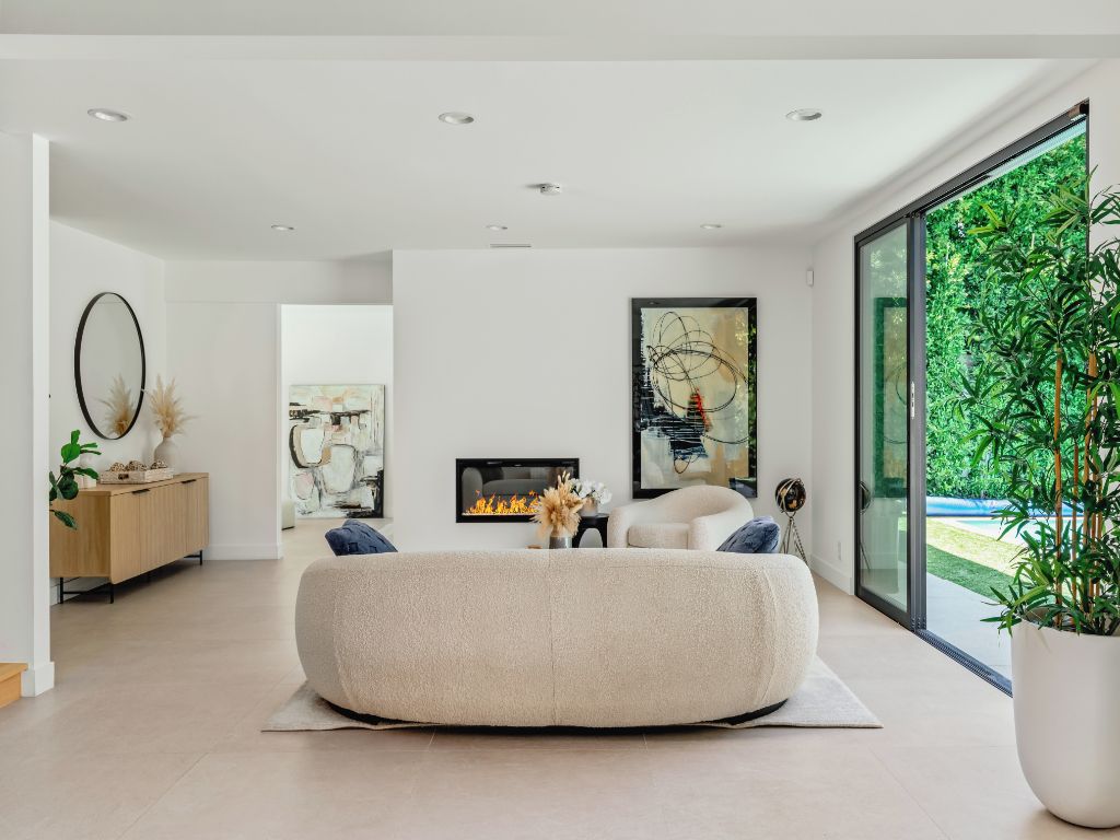 Una sala de estar moderna con un enorme sillón de girable, una chimenea y un ventanal con vistas a la vegetación.