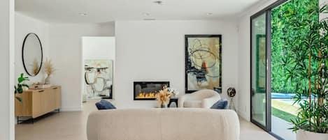 Una sala de estar moderna con un enorme sillón de girable, una chimenea y un ventanal con vistas a la vegetación.