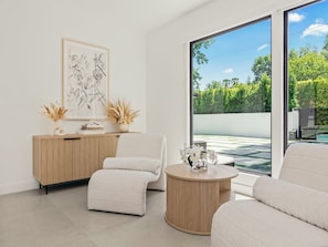 A modern living room with a large window, a wooden cabinet, a round coffee table, and a beige sofa. - Casa Leona (Encino)