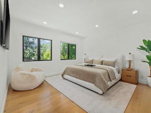 A modern bedroom with a large bed, a bean bag chair, and a bedside table with a lamp. - Casa Leona (Encino)