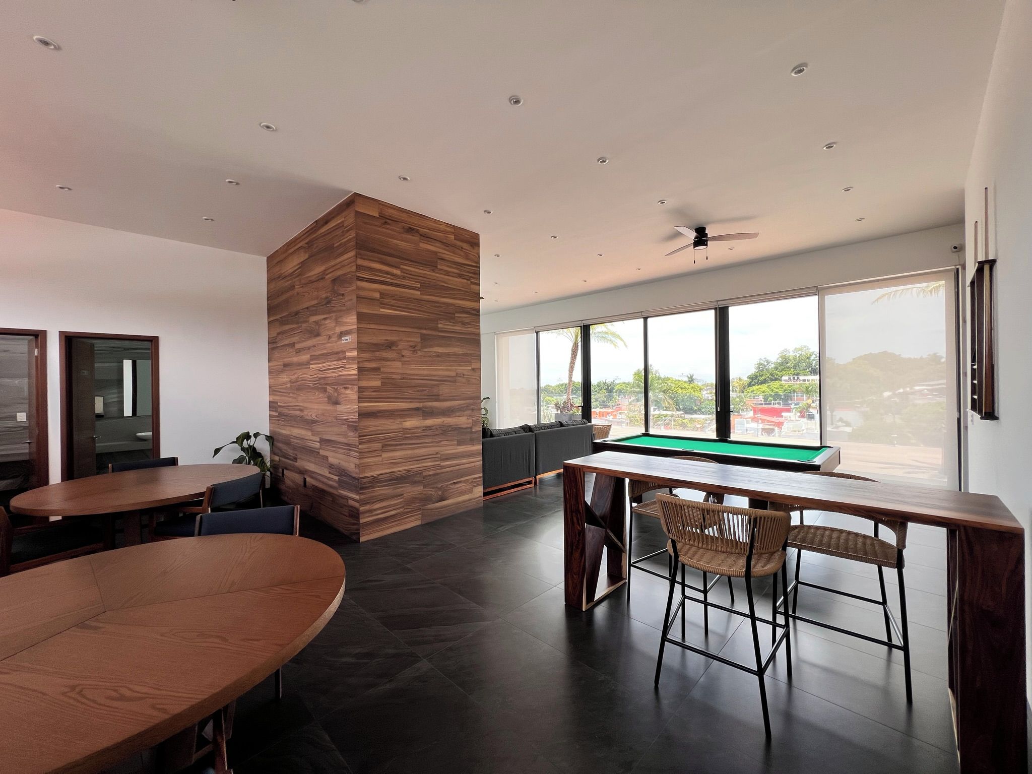 A modern indoor space with a pool table, wooden furniture, and large windows offering a view.