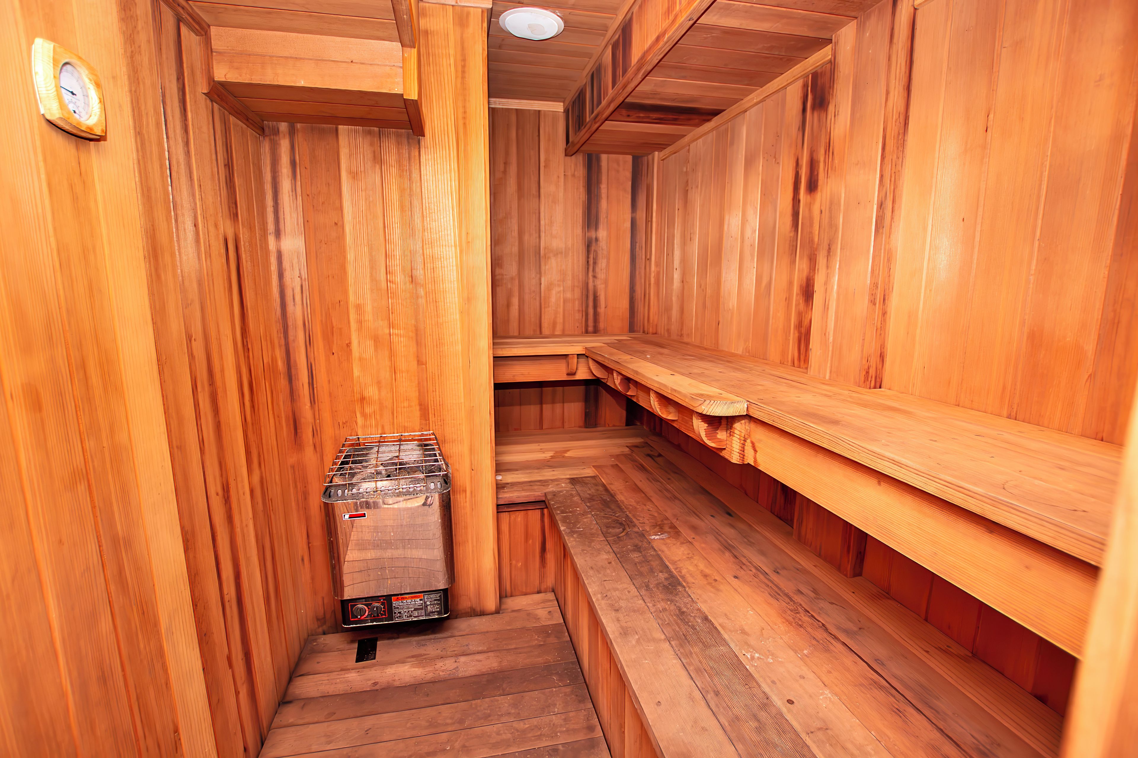 A sauna with wooden walls and benches, a sauna heater, and a wall-mounted thermometer.