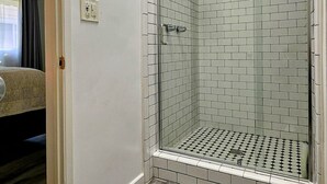 Et brusebad med glasdør, trægulv og en loftlampe.
