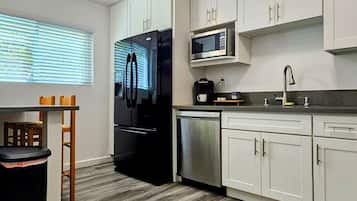 Una cucina moderna con mobili bianchi, un frigorifero nero, un forno a microonde e una lavastoviglie in acciaio inossidabile.