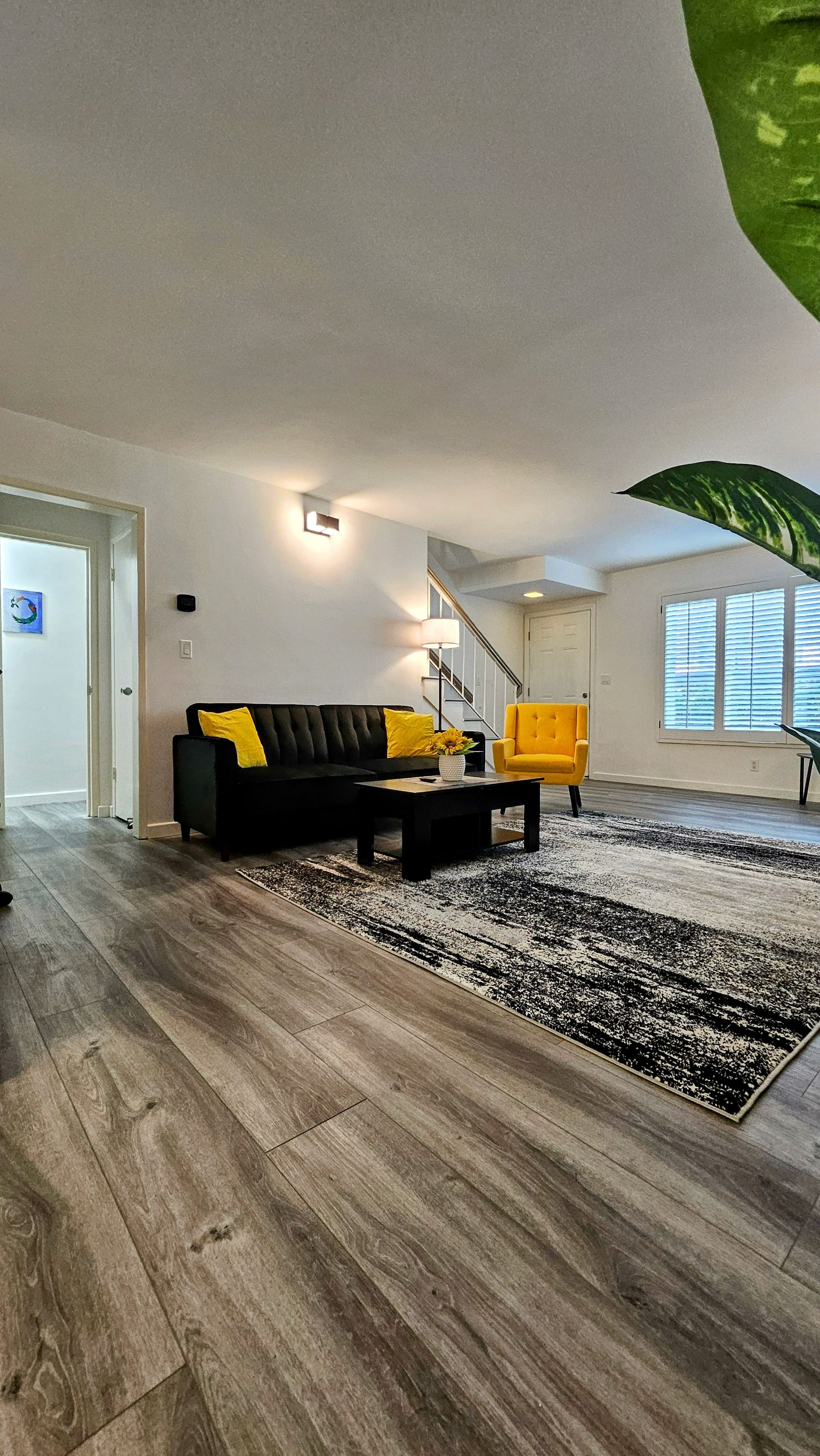 A modern living room with a black sofa, yellow cushions, a coffee table, and a large green plant.