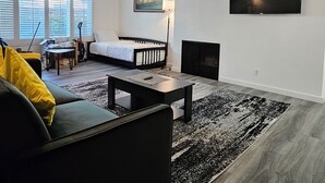 En moderne stue med sofa, sofabord, pejs og et tv ophængt på væggen.