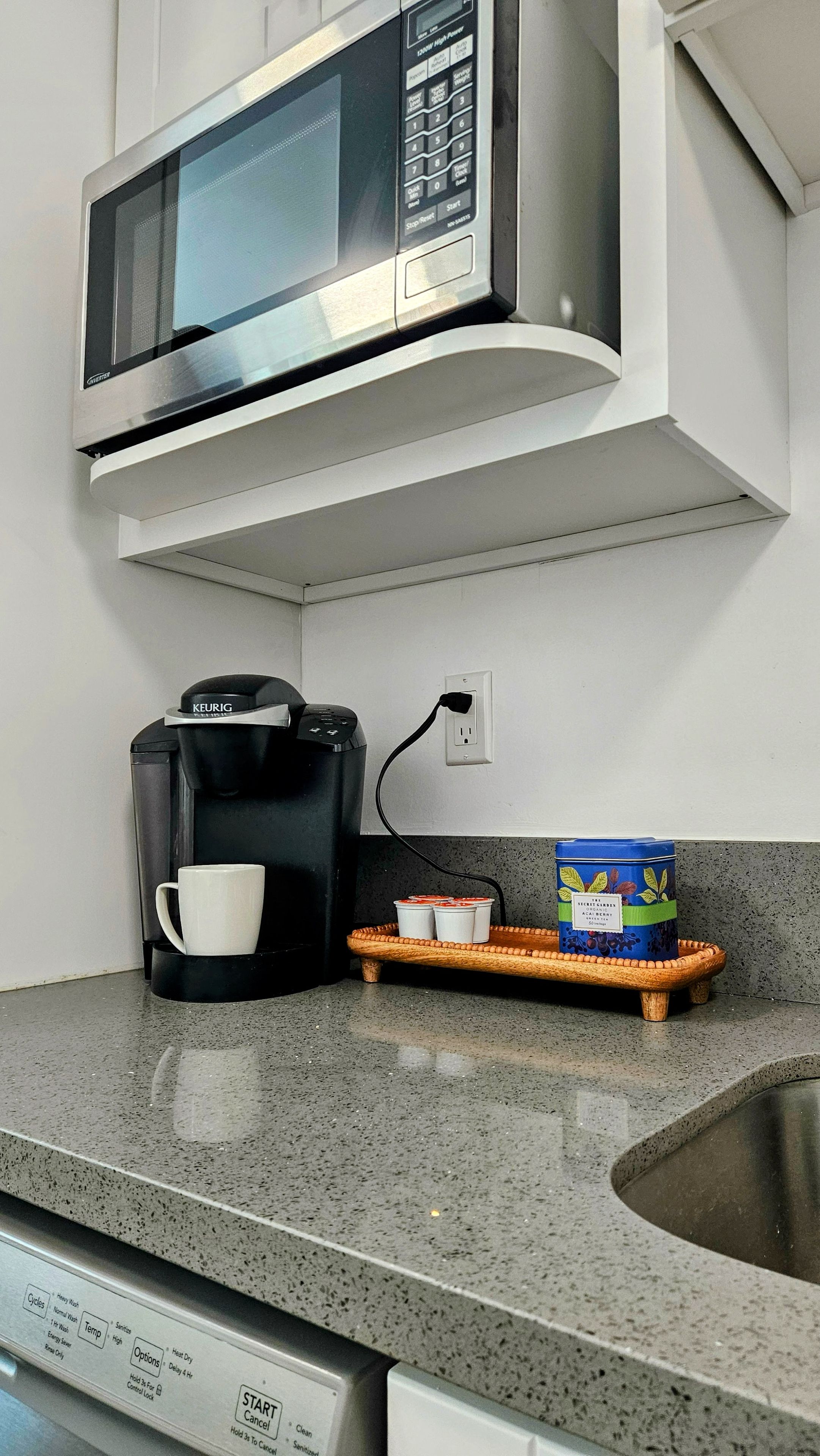 Een keuken met een magnetron, koffiezetapparaat en een dienblad met bekers en een bak.