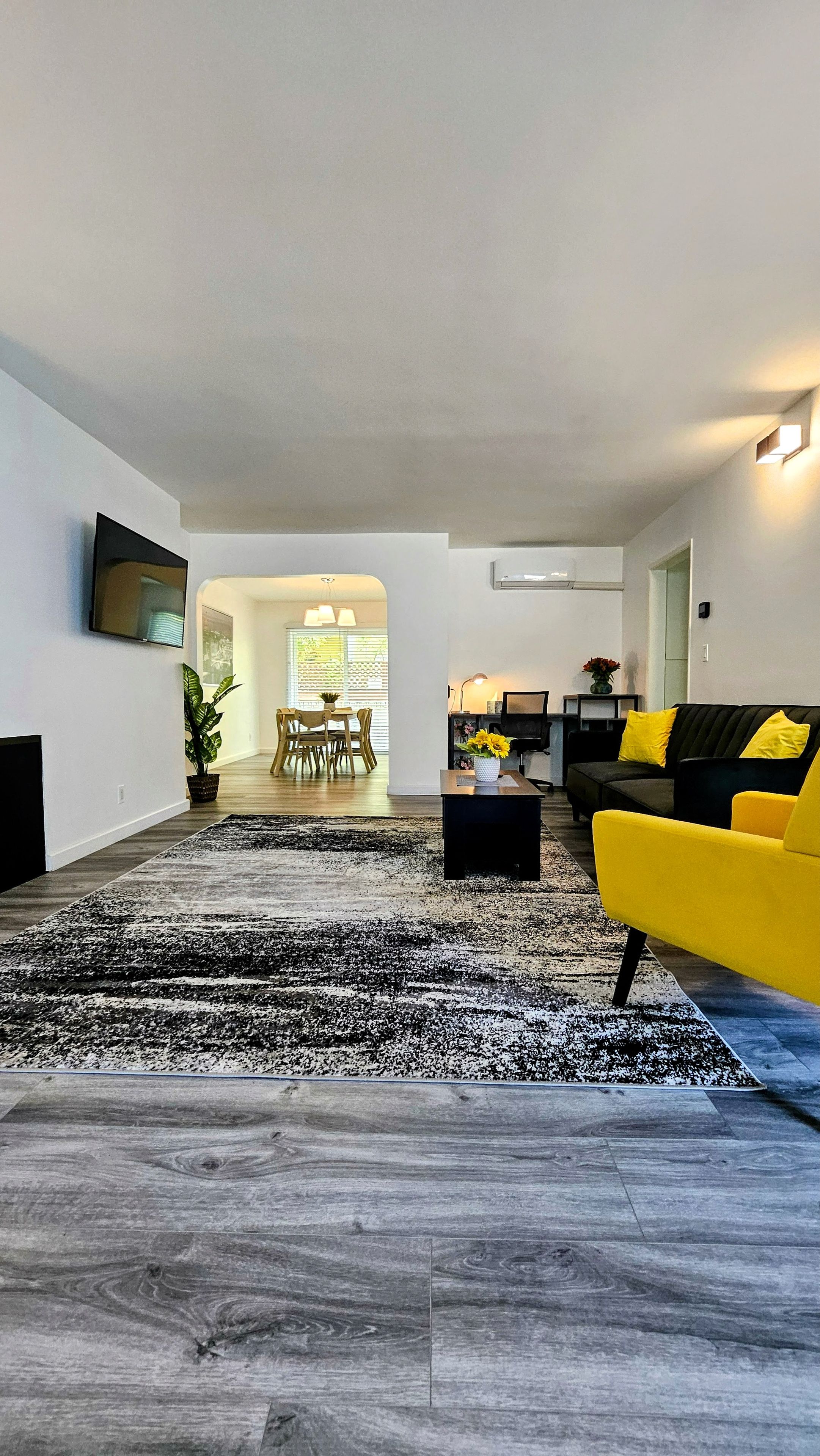 Ein modernes Wohnzimmer mit einem schwarz-weißen Teppich, einem gelben Sofa und einem Essbereich im Hintergrund.