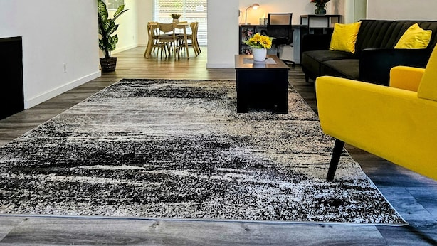 En moderne stue med et sort-hvidt tæppe, en gul sofa og et spiseområde i baggrunden.