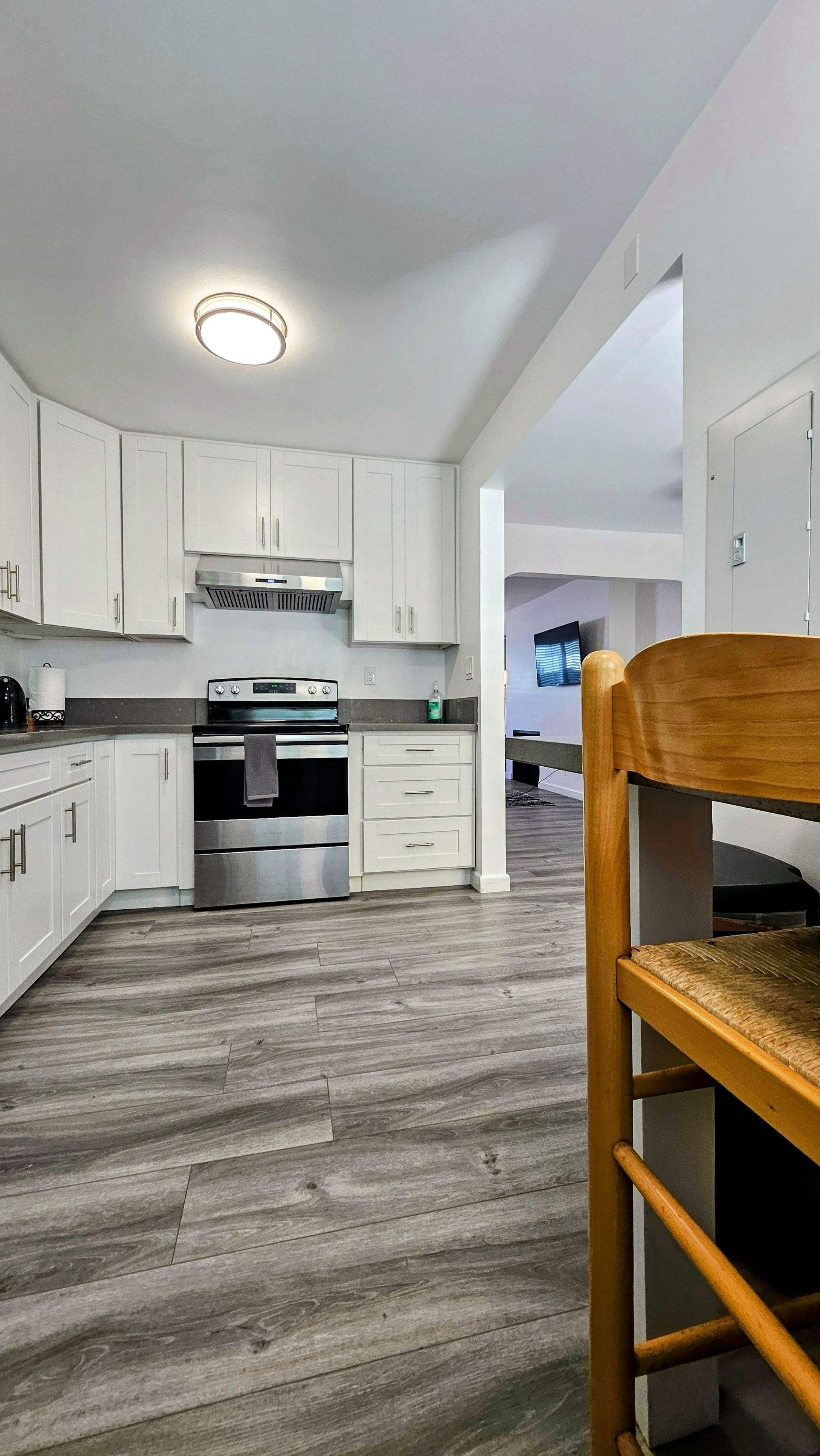 A modern kitchen with white cabinets, stainless steel appliances, and a wooden floor.