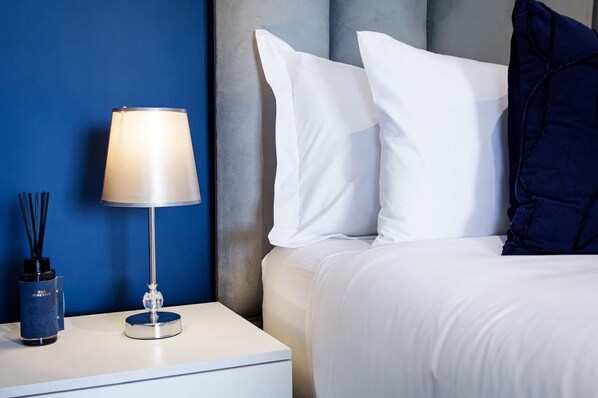 A neatly made bed with white bedding, a bedside lamp, and a blue wall.