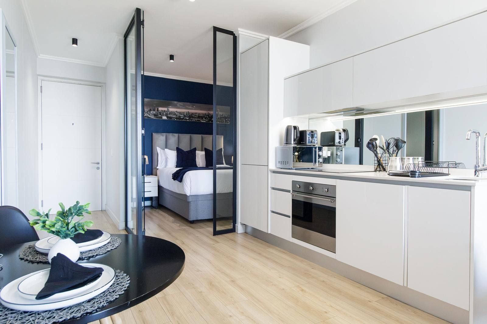A modern apartment with a kitchen, dining area, and a bedroom with a cityscape view.