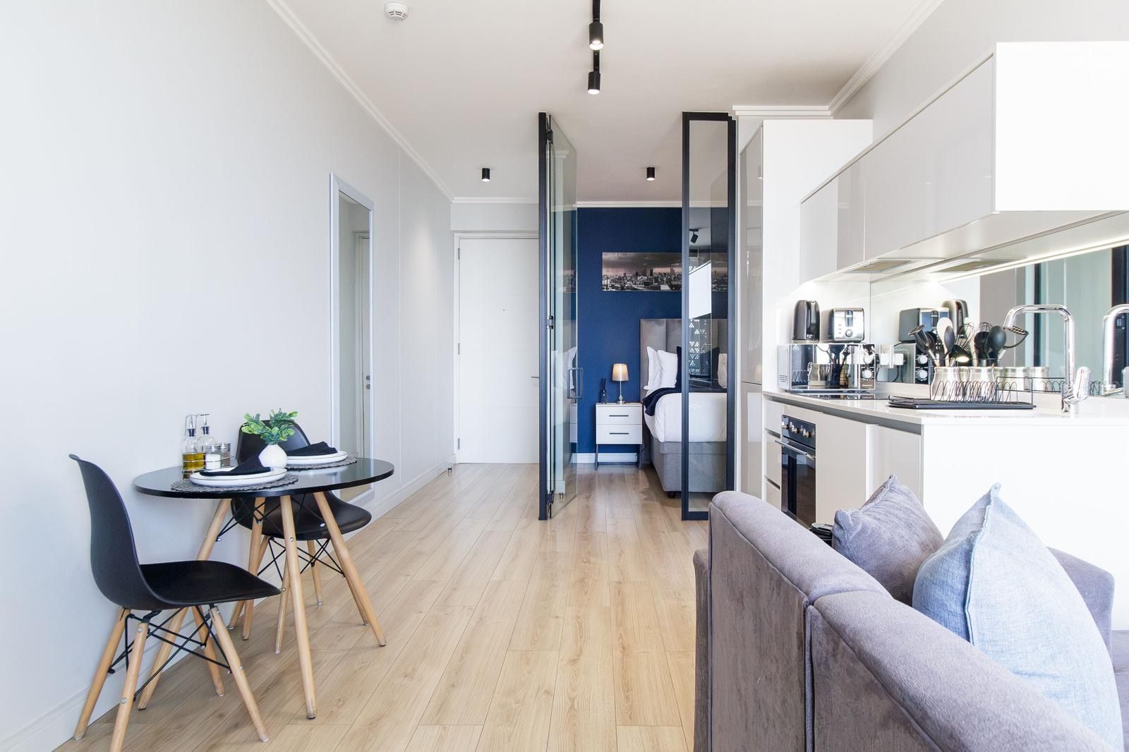 A modern kitchen with a dining area, a sofa, and a bed in the background.