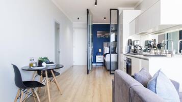 A modern kitchen with a dining area, a sofa, and a bed in the background.