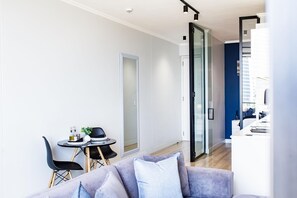 A modern living room with a sofa, a dining table with chairs, and a glass door leading to a kitchen area.