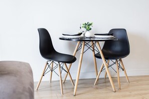 A dining area with a round table, two black chairs, a small white vase with a plant, and a bottle of oil.