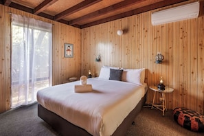 Een slaapkamer met een groot bed, een nachtkastje met een lamp, een wandairconditioner en een raam met dunne gordijnen.