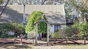 A rustic building with a corrugated metal roof, surrounded by greenery and a wooden fence. - New: Quitch Cottage - steps from the beach (Quindalup)