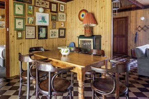 Een kamer met houten lambrisering en een geruit vloerkleed, een houten eettafel met stoelen en diverse ingelijste foto's aan de wanden.