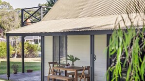 A covered outdoor seating area with a table and chairs, a potted plant, and a view of the surrounding greenery. - New: Quitch Cottage - steps from the beach (Quindalup)