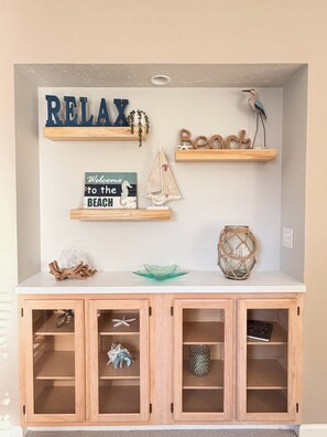 A wall with shelves displaying various beach-themed decorations, including a sign that says 'RELAX' and another that says 'Welcome to the BEACH.' - Coastal 2B condo minutes from the beach & attractions with pool and golf access! (Longs)